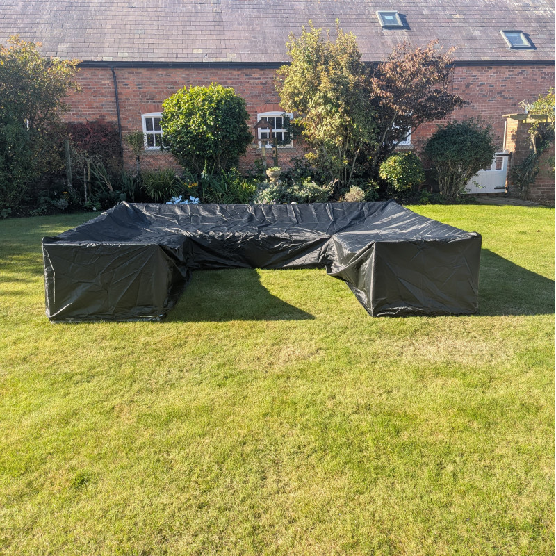 A large black tarpaulin covering a rectangular structure on grass, set against a garden background with trees and walls.