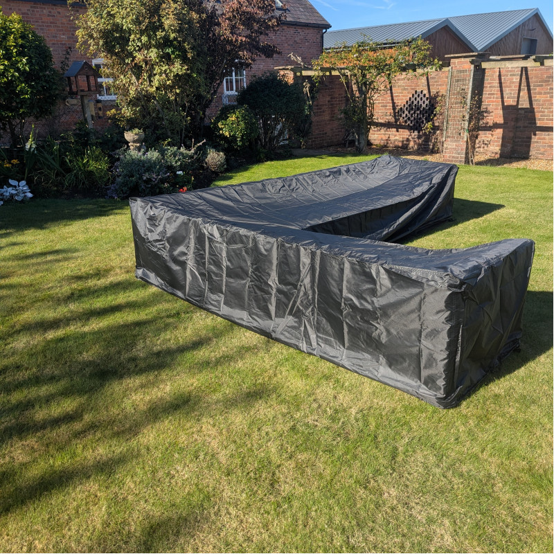 A large black tarpaulin covering a rectangular structure on grass, set against a garden background with trees and walls.