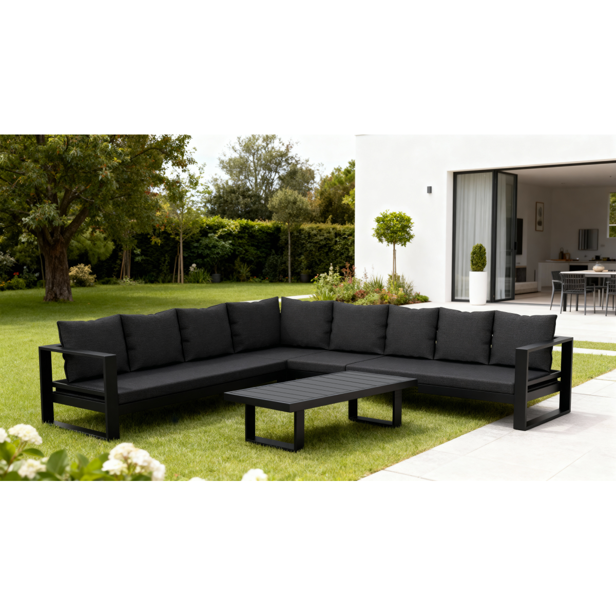 Outdoor seating area with a glass-top fire pit, surrounded by red and white patterned cushions on dark grey sofas, and green lawn.