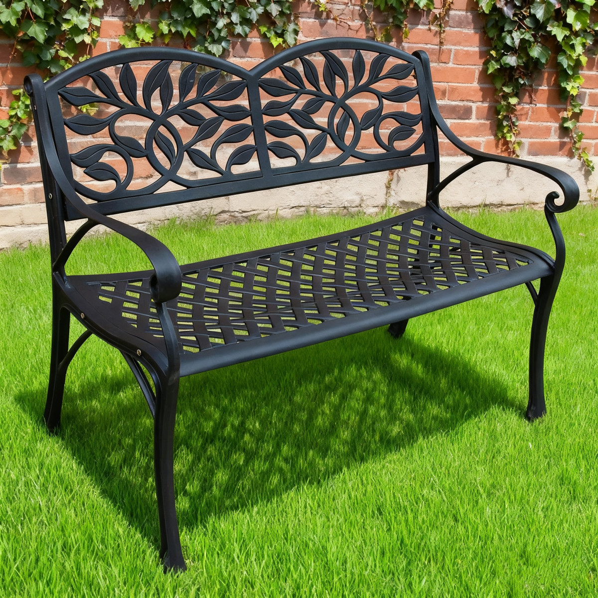 A white metal garden bench with ornate leaf patterns, positioned on a grassy area surrounded by flowers.