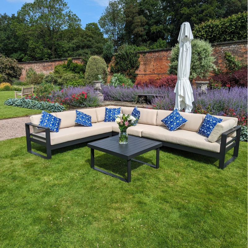 Garden seating area featuring a dark sofa with red patterned cushions, a glass vase of flowers on a table, and a parasol.
