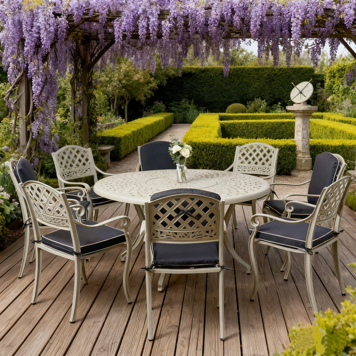 Outdoor dining table set with a white pitcher, wine bottle, glasses, and bowls, surrounded by green grass and flowers.