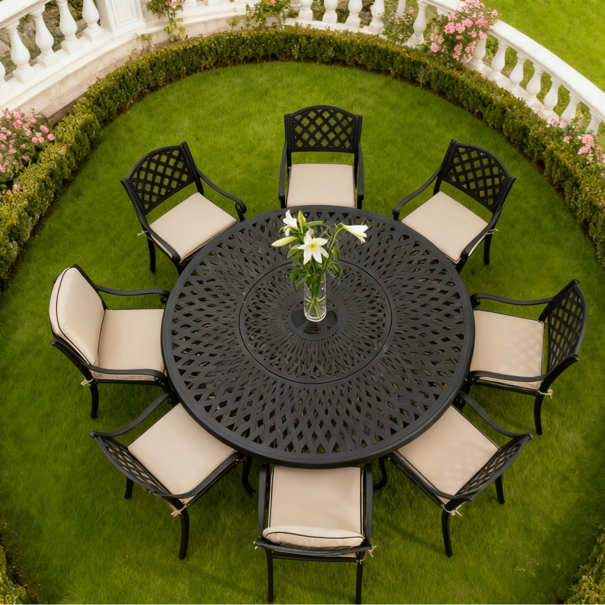 A round garden table surrounded by eight white cushioned chairs, featuring a vase of green flowers and wine glasses.