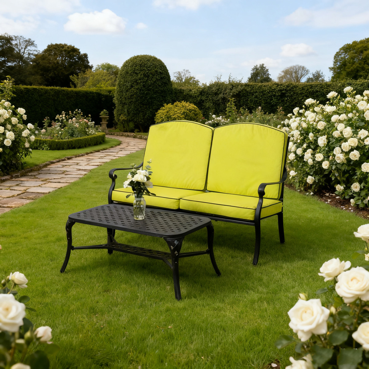 Black cushioned bench behind an ornate iron table with a white pitcher of colourful flowers, set on gravel garden.