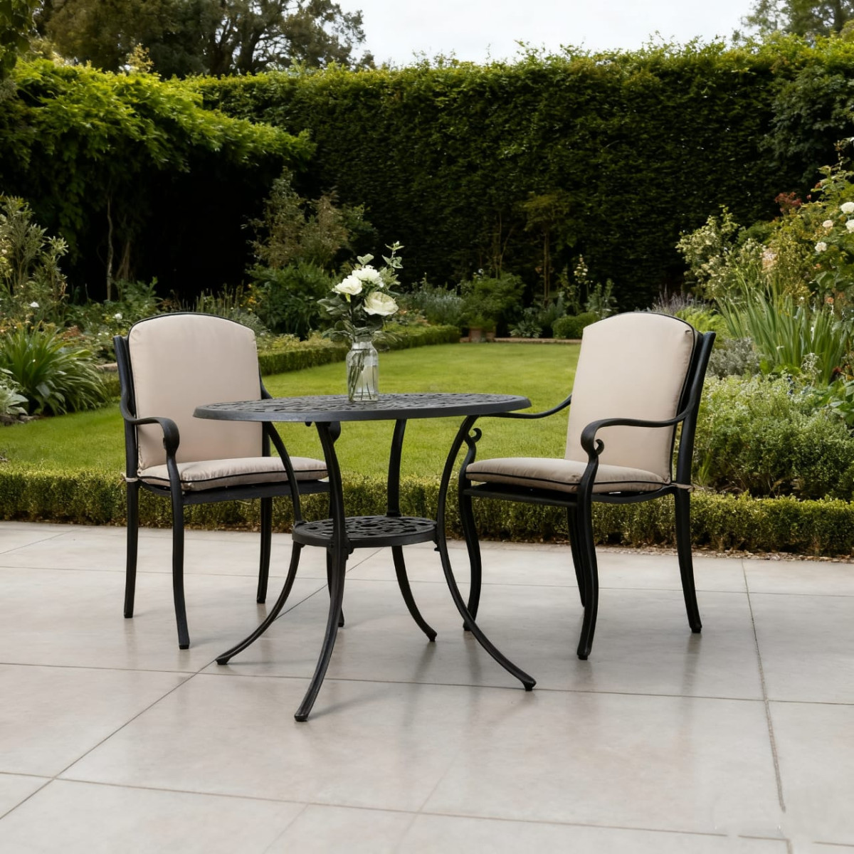 Round, patterned table set in a garden, with two empty bowls and plates placed on it, surrounded by lush flowers.