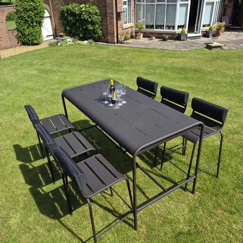 A garden table with four chairs, wine bottle, and glasses, surrounded by greenery and flowers on a sunny day.