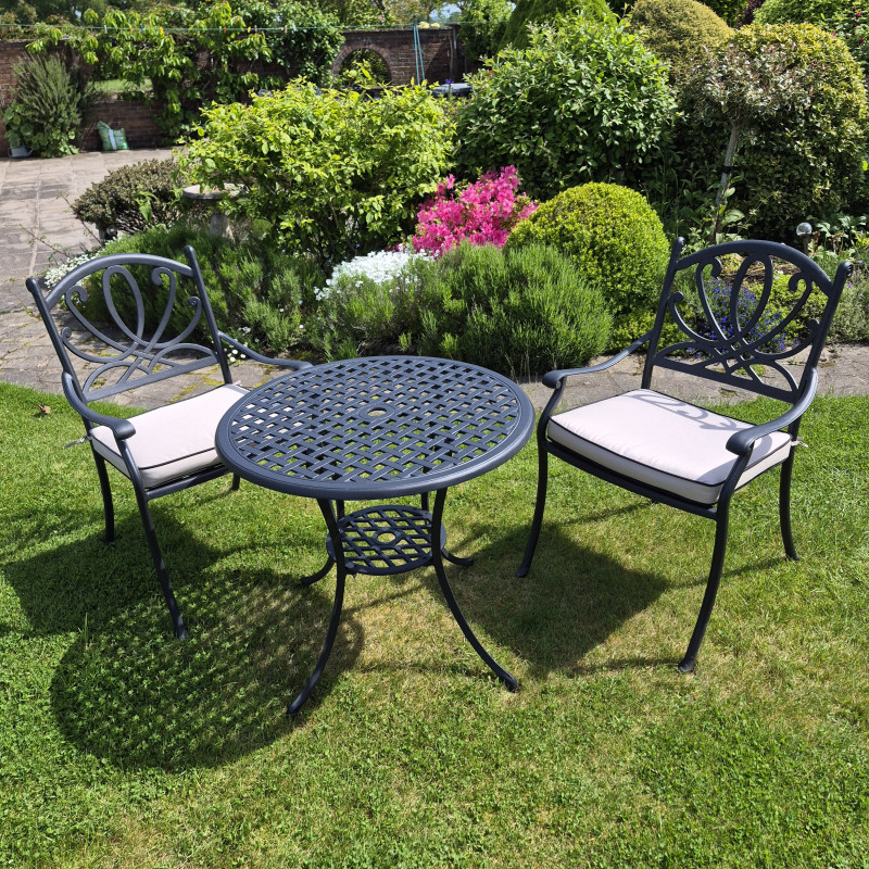 Black metal table with two chairs on a green lawn, against a brick wall covered in leafy vines.