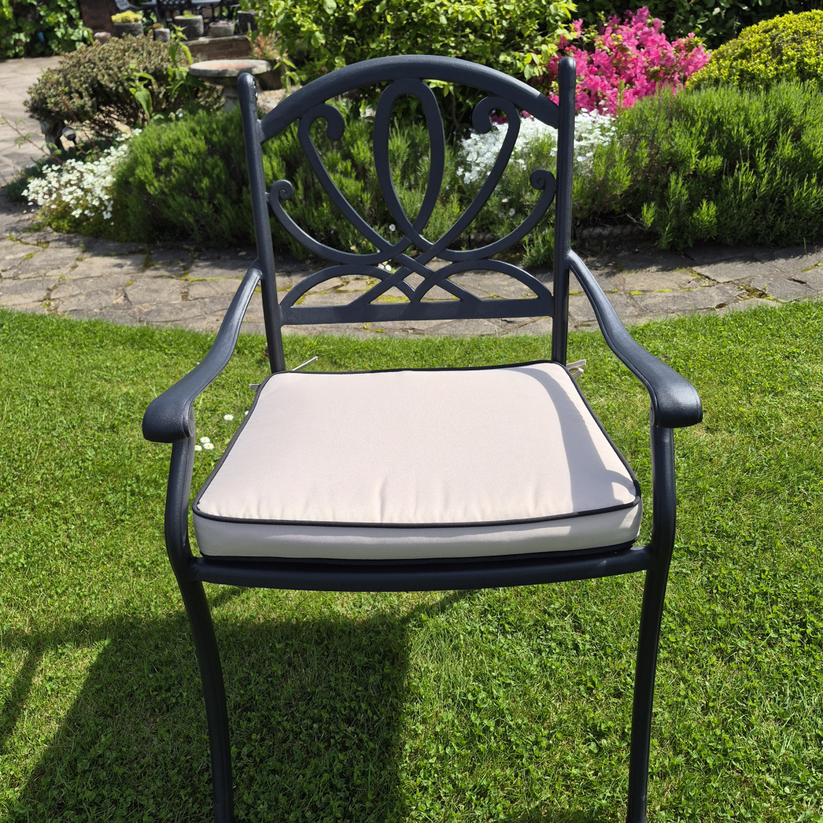 Two black metal chairs with green cushions flanking a round table, set on a grassy area against a white brick wall.