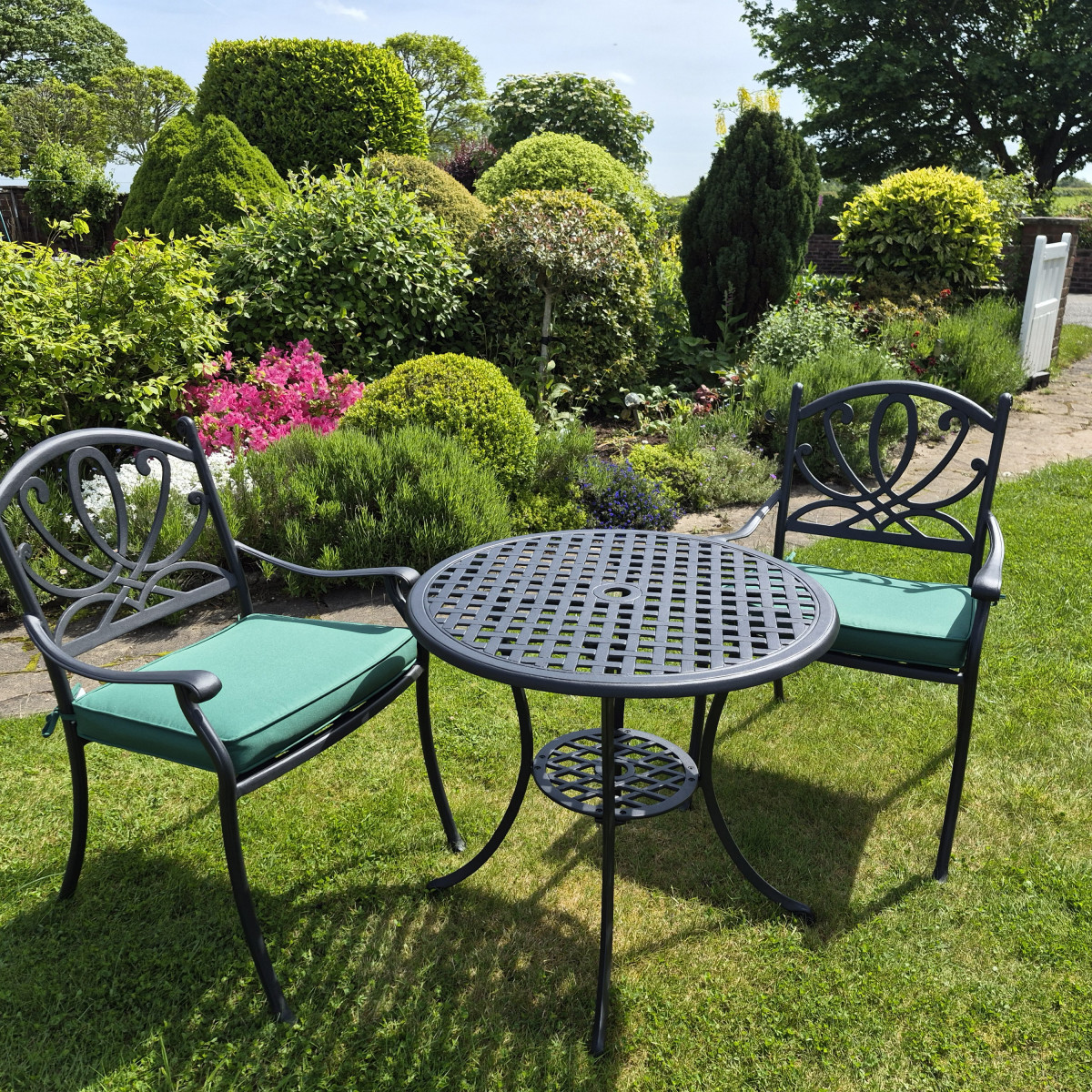 Black metal table with two chairs on a green lawn, against a brick wall covered in leafy vines.