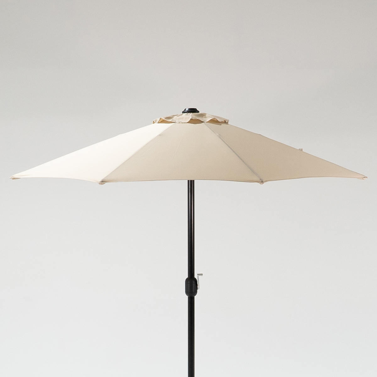 A cappuccino coloured, eight-panel parasol with a black pole, standing upright against a light grey background.