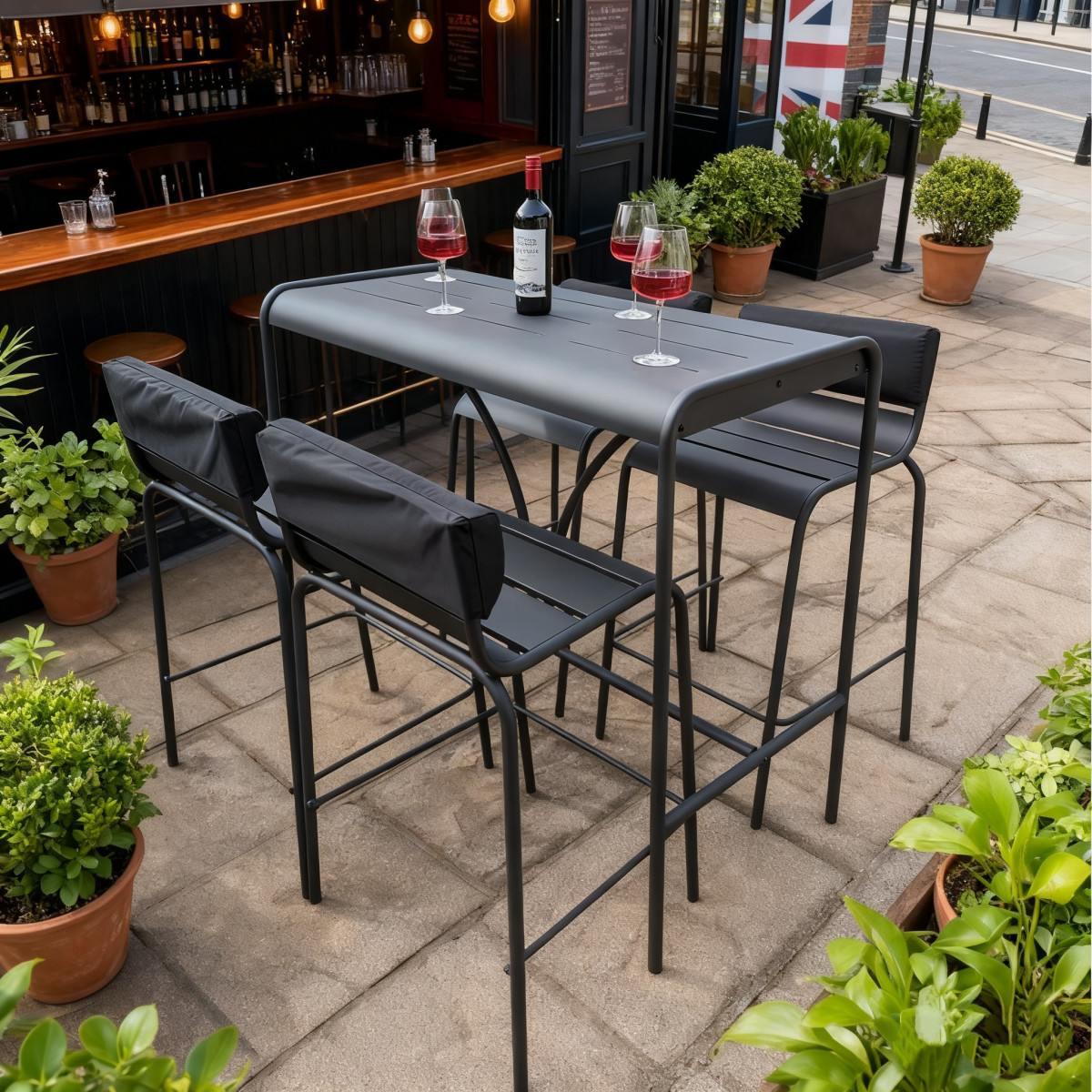 A garden table with four chairs, wine bottle, and glasses, surrounded by greenery and flowers on a sunny day.