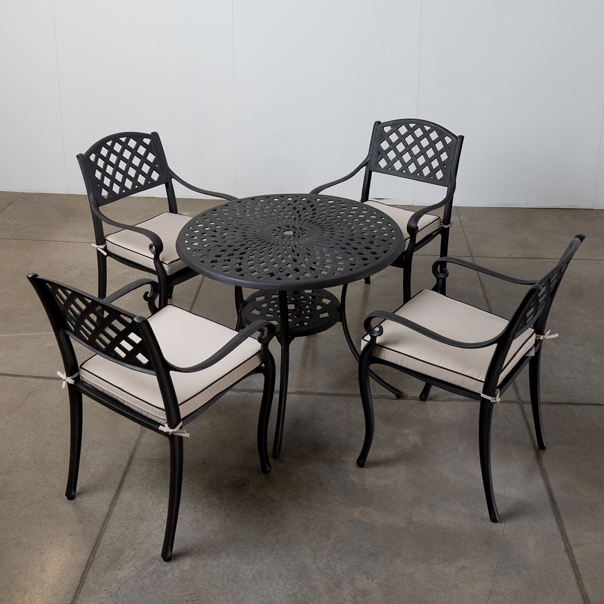 A garden table set with four chairs, an umbrella, a wine bottle, glasses, and floral plants in a green lawn setting.